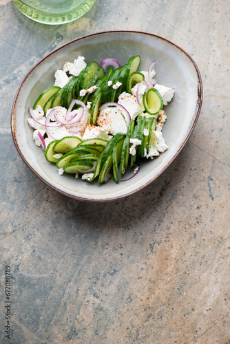 Bowl of cucumber and feta cheese salad on a beige and grey granite background, vertical shot with space, high angle view