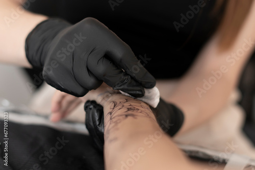 a woman tattooist removes excess ink from skin with white cotton pad