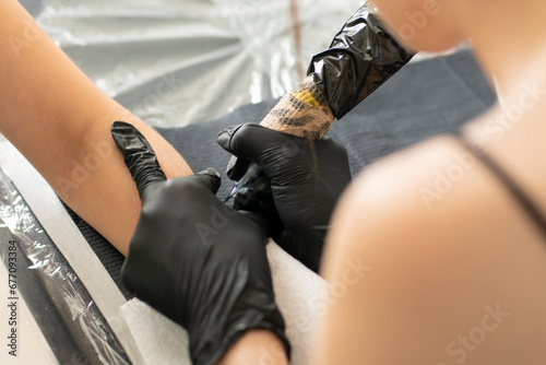 a female master tattoo artist in black gloves making a tattoo to a client photo