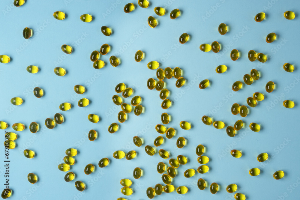 Close up of oil filled capsules suitable for: fish oil, omega 3, omega 6, omega 9, vitamin A, vitamin D, vitamin D3, vitamin E. Many capsules on blue background. Top view, flat lay. Banner. Close up of oil filled capsules suitable for: fish oil, omega 3, omega 6, omega 9, vitamin A, vitamin D, vitamin D3, vitamin E. Many capsules on blue background. Top view, flat lay. Banner.