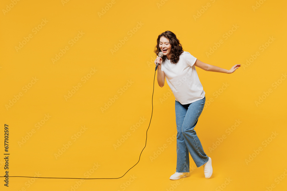 Full body singer happy fun young woman wear white blank t-shirt casual clothes sing song in microphone at karaoke club isolated on plain yellow orange background studio portrait. Lifestyle concept. - obrazy, fototapety, plakaty 