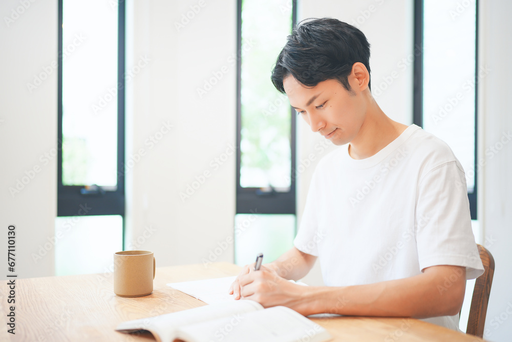 自宅のリビングで資格取得のために勉強する若い男性 自宅のリビングで資格取得のために勉強する若い男性