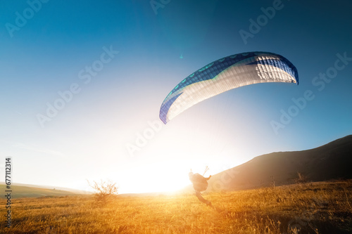 Launching a speedwing from a mountain. A paraglider is preparing to take off from a mountain, running along the yellow autumn grass against the sun