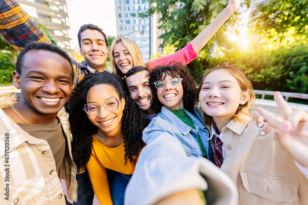 Obraz premium Young community of diverse happy student friends taking selfie portrait together. Millennial group of people having fun enjoying free time outdoors. Youth, diversity and friendship concept.