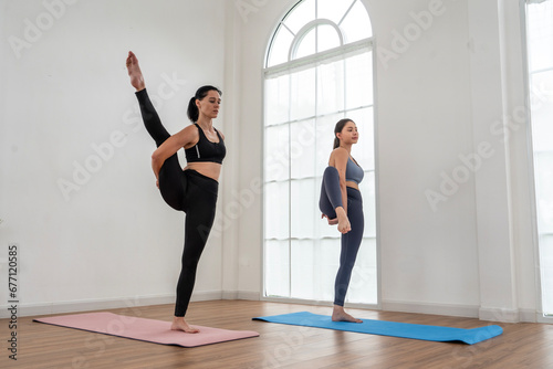 woman exercising with a yoga instructor wearing sports clothes practices yoga class and poses while stretching together in a home living room. Health, lifestyle and exercise concepts