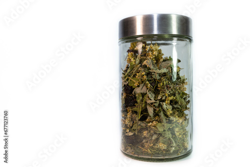 Mix of green herbs, plants used for tea in a glass jar isolated on white background.