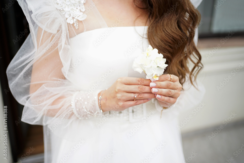 The bride is standing by the window, holding a wedding boutonniere in her hands. Preparation for the wedding ceremony. The bride is standing by the window, holding a wedding boutonniere in her hands. Preparation for the wedding ceremony.
