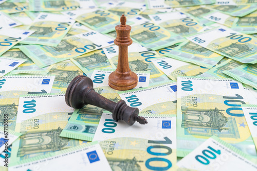 Chess pieces on multiple 100 euro bank notes. Black king down, white king standing. Concept of stock market competition.