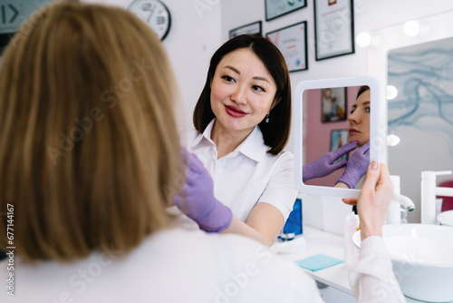 Positive Asian female cosmetician preparing patient for procedure