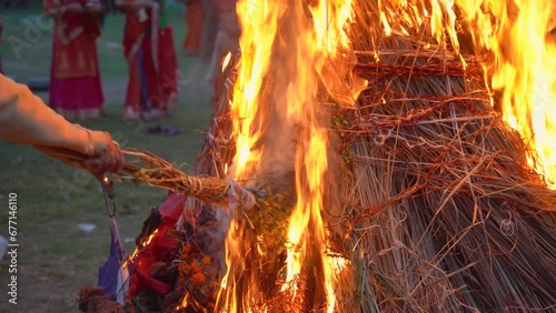 slow motion shot showing hand roasting wheat gram beans over fire on hindu festival of holi lohri with people dancing around a huge bonfire photo