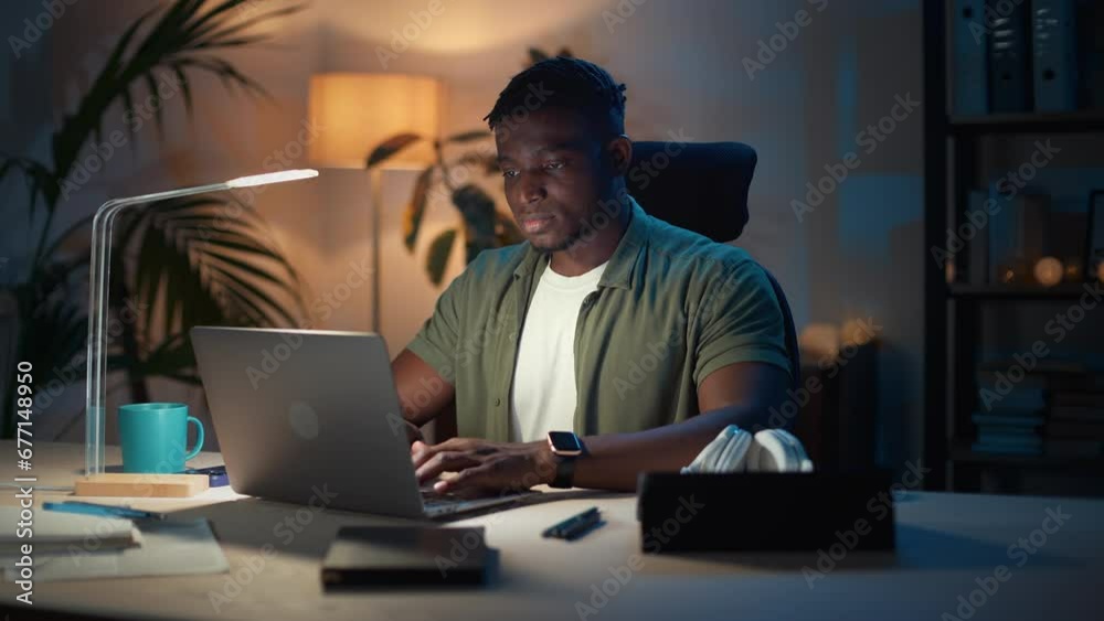 Busy african man typing on laptop at home during evening Busy african man typing on laptop at home during evening
