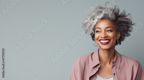 Fashionable woman with curly grey hair laughing against a cool-toned backdrop