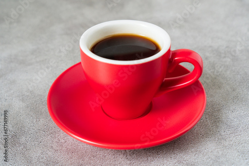 Close-up shot of red doppio normale ceramic 80ml or 2oz espresso cup with saucer placed on loft industrial style old cement dining table, the black espresso coffee is in the cup. © MU Studio