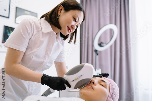 Smiling Asian woman applying facial procedure in clinic