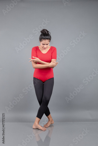 Healthy young woman in red t-shirt and black leggings doing yoga and stretching exercises isolated on grey background © Anupam