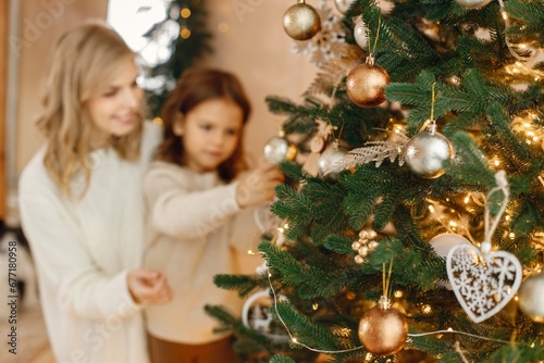 Little girl and her mom having fun near Christmas tree together