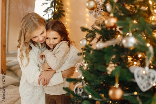 Little girl and her mom having fun near Christmas tree together