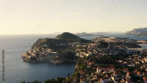 Drone flies over Dubrovnik Croatia during a summer sun set with coastal mountain side and islands in distance - 4k