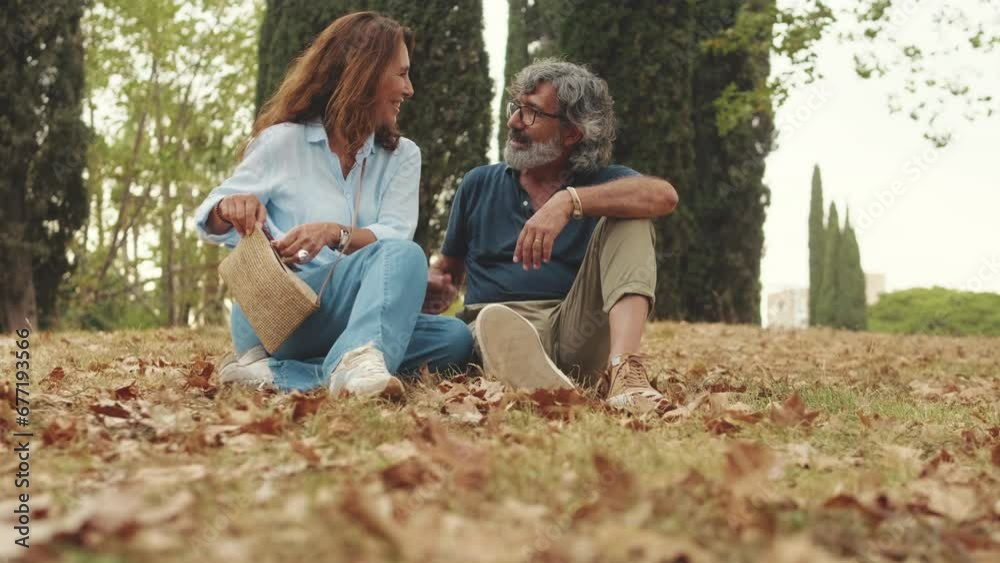 Elderly couple chatting while sitting on the grass in the park Elderly couple chatting while sitting on the grass in the park
