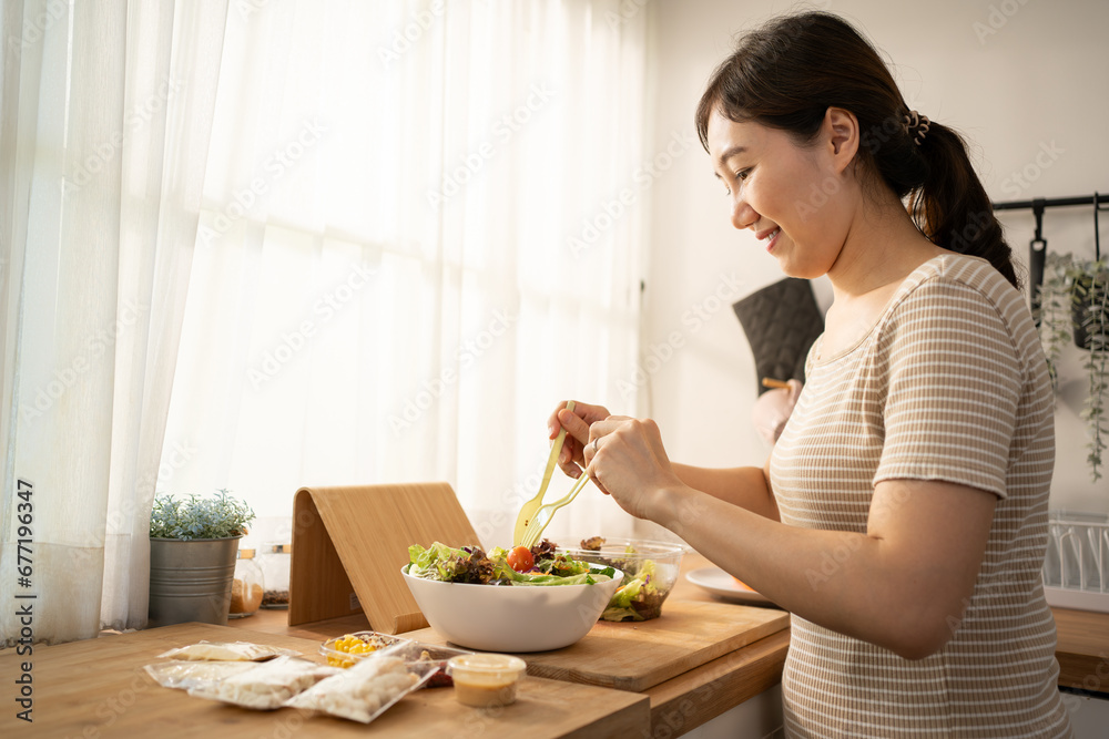 Happy smiling young Asian woman is preparing a fresh healthy vegan salad with many vegetables in the kitchen at home and trying a new recipe. Happy smiling young Asian woman is preparing a fresh healthy vegan salad with many vegetables in the kitchen at home and trying a new recipe.