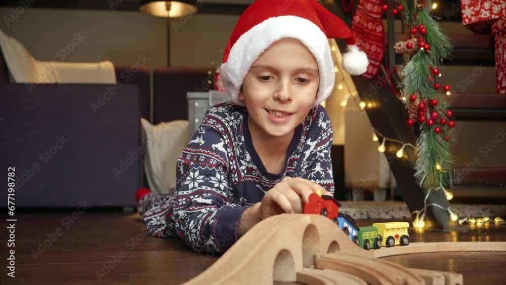 Portrait of happy little boy celebrating Christmas lying on floor and playing with colorful wooden train and wooden railroad. Winter holidays, celebrations and party Portrait of happy little boy celebrating Christmas lying on floor and playing with colorful wooden train and wooden railroad. Winter holidays, celebrations and party