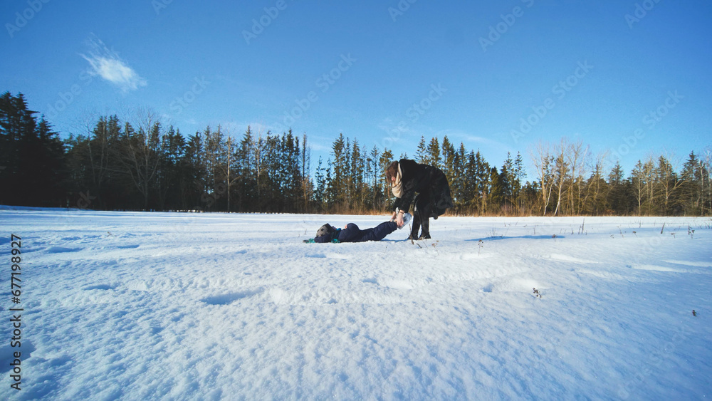 A mother drags her son through the snow while playing.