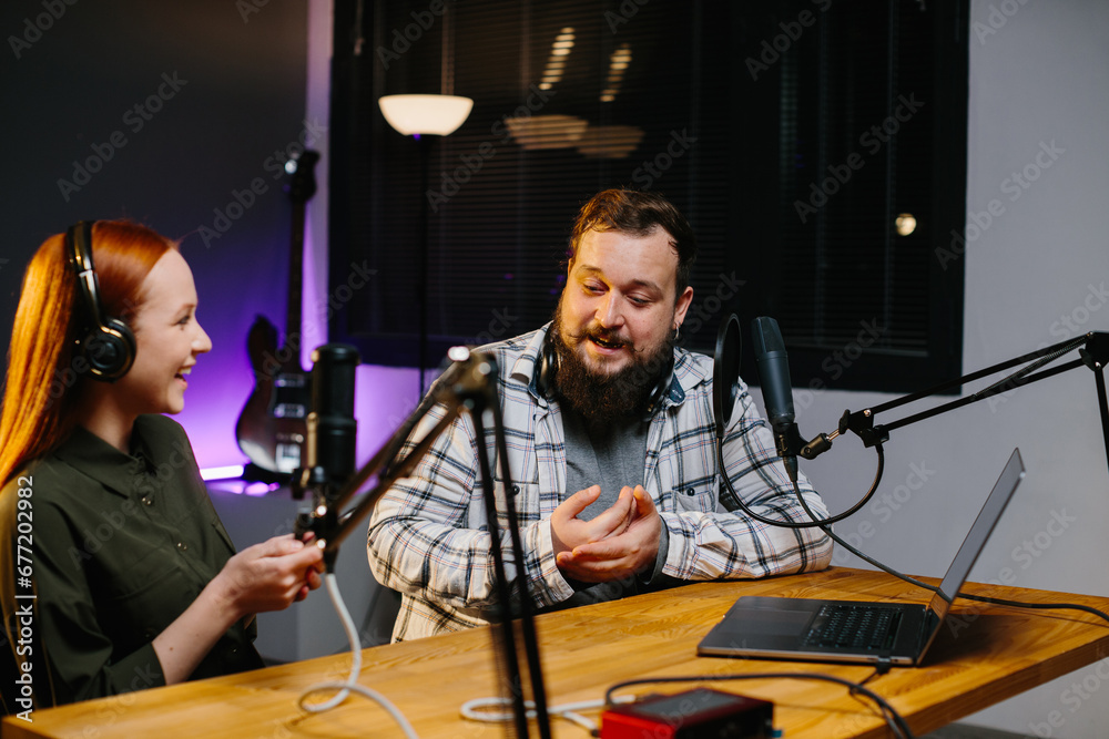 An online show host records a podcast with a guest in a home studio. Happy man and woman laughing together during internet streaming session. An online show host records a podcast with a guest in a home studio. Happy man and woman laughing together during internet streaming session.