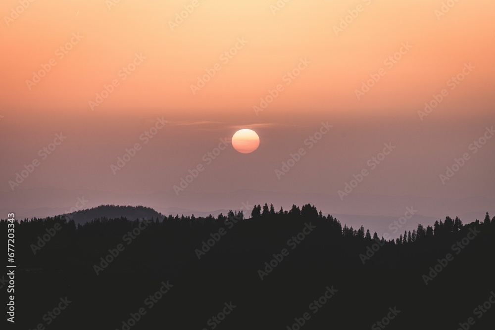 Beautiful sunset scenery in the calm sky over silhouettes of hills and trees