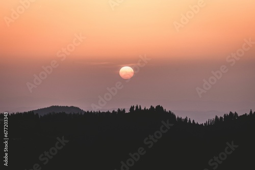 Beautiful sunset scenery in the calm sky over silhouettes of hills and trees