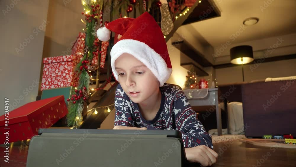 Closeup of little boy celebrating Christmas lying on floor and playing video games on tablet computer. Winter holidays, celebrations and party Closeup of little boy celebrating Christmas lying on floor and playing video games on tablet computer. Winter holidays, celebrations and party