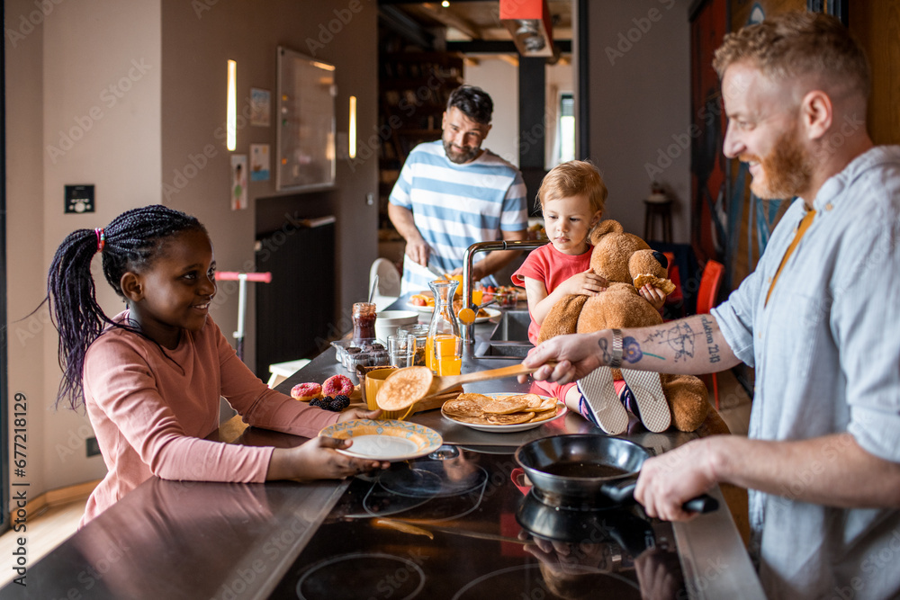Male gay couple with children making breakfast in the kitchen Male gay couple with children making breakfast in the kitchen