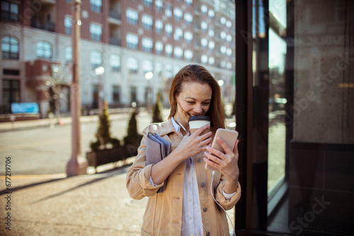 Smiling young woman with coffee cup using smartphone in the city © Vorda Berge