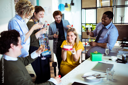 Young woman celebrating birthday holding cake with colleagues in office