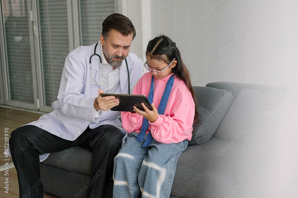 Pediatrician doctor talking to kids with tablet in medical clinic. Male doctor to check up health children in examination hospital room. Healthcare and medical Kids concept. Pediatrician doctor talking to kids with tablet in medical clinic. Male doctor to check up health children in examination hospital room. Healthcare and medical Kids concept.