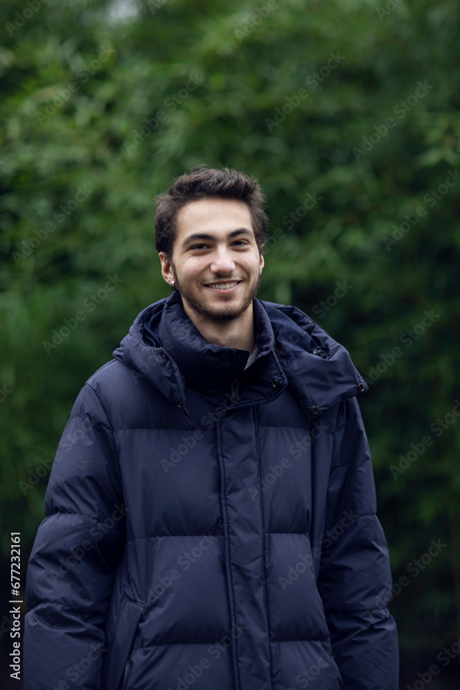 Portrait of a smile handsome young man in park, wear in warm clothes, tree background.