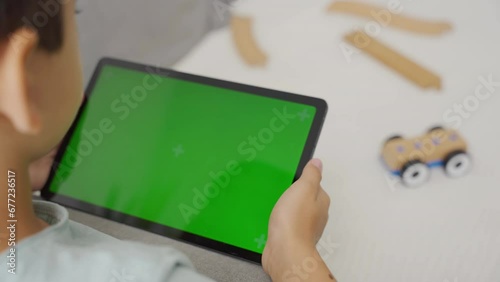 Kid boy gaming or using social media on tablet with chroma key background. 