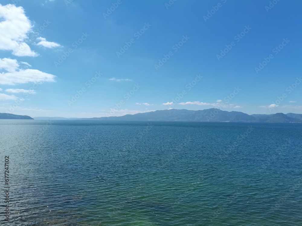 Breathtaking view of big blue lake under blue cloudy sky with mountains in the background