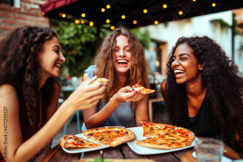 Three happy female friends eating pizza in restaurant