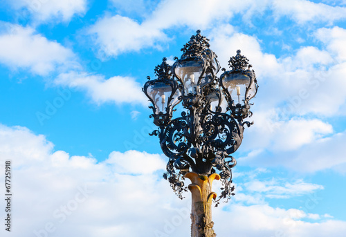 Obraz na płótnie Street lamp against the blue sky with clouds . Lamp base features elaborate scrolls and curves, characteristic of the Baroque period w salonie