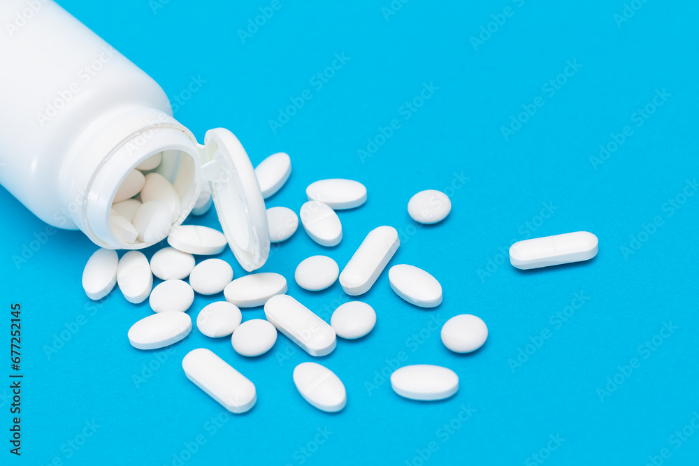 Global Pharmaceutical Industry and Medicinal Products - White Pills or Tablets Scattered from the Pill Container, Lying on Blue Background Global Pharmaceutical Industry and Medicinal Products - White Pills or Tablets Scattered from the Pill Container, Lying on Blue Background