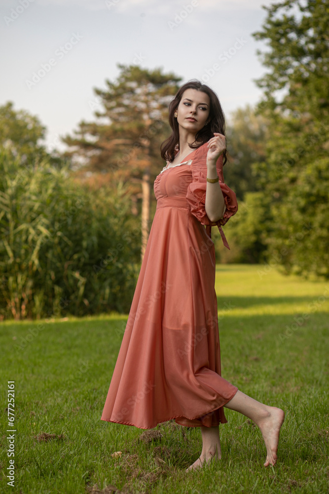 Portrait of a beautiful brunette girl in dress dancing in the park, tree background.
