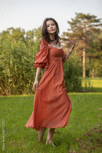 Portrait of a beautiful brunette girl in dress dancing in the park, tree background. 