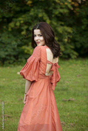 Portrait of a beautiful brunette model in pretty dress posing in the park, tree background. 