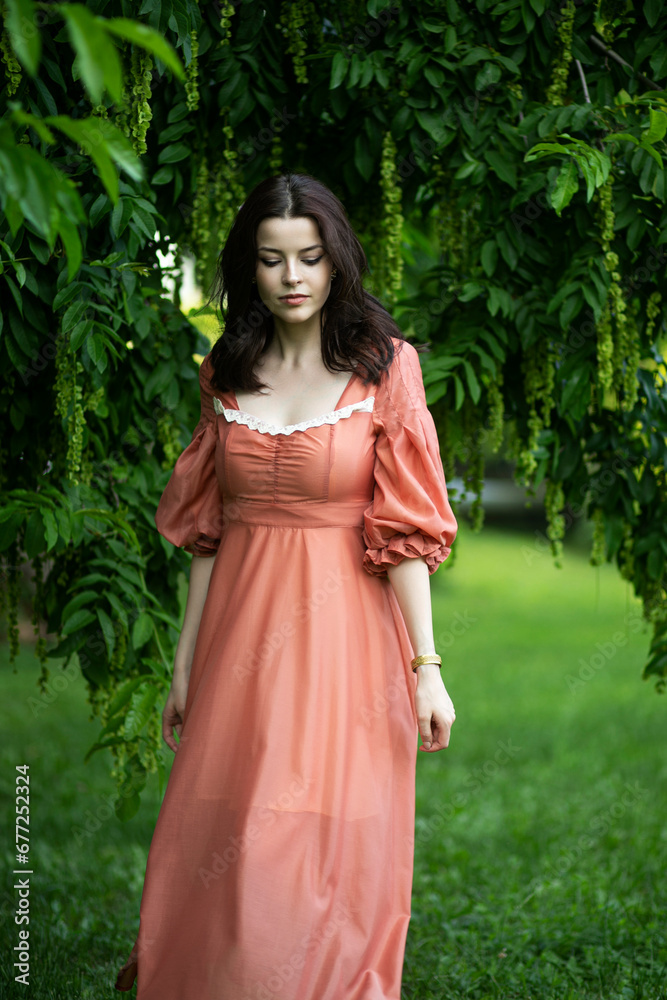 Portrait of a beautiful brunette girl in dress walking in the park, tree background.
