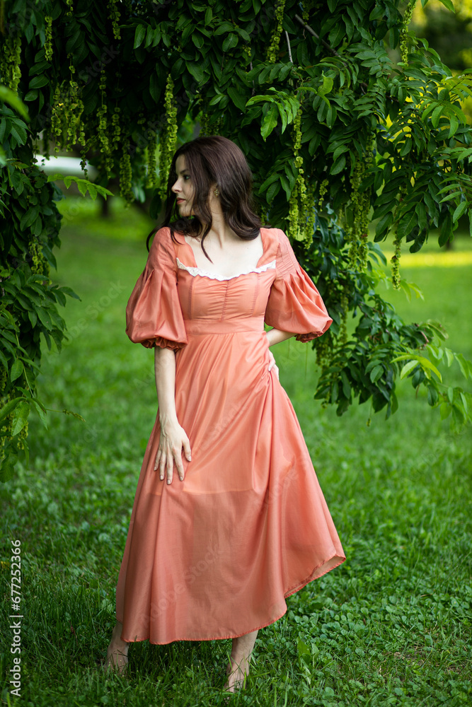 Side view of a beautiful brunette girl in dress posing in the park, tree background.
Side view of a beautiful brunette girl in dress posing in the park, tree background.