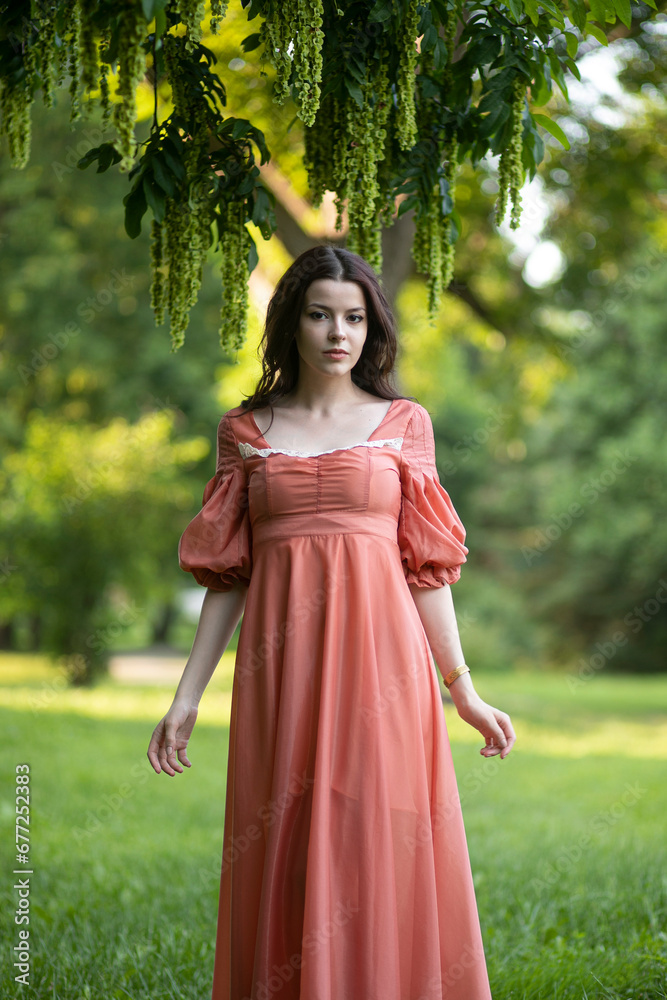 Portrait of a beautiful girl in dress posing in the park, tree background.
Portrait of a beautiful girl in dress posing in the park, tree background.