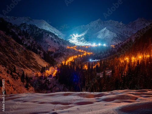 Night panorama of the illuminated serpentine road and the Chimbulak ski resort. Late winter evening high in the mountains