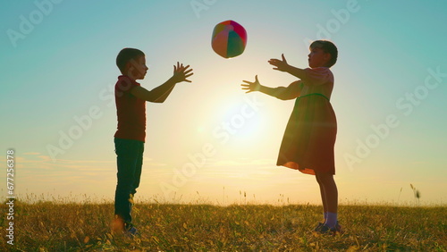 Children play with big ball in park against backdrop of sun. Happy child throws ball with his hands. Kids, boy, girl have fun with ball in park at sunset. Sports games for children outdoors. Family photo