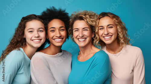 Four happy women of different ages and ethnic backgrounds, with bright smiles, posing together against a vibrant blue background. photo