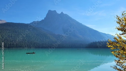 Landscape view of the fir forest trees and mountains near the lake against a blue sky © Wirestock